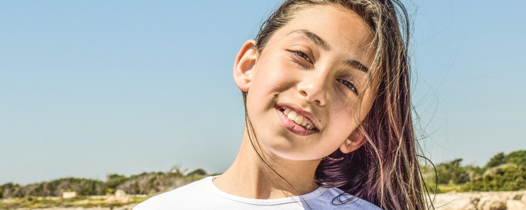 Smiling young girl with visible dental alignment, showcasing functional orthodontic results outdoors