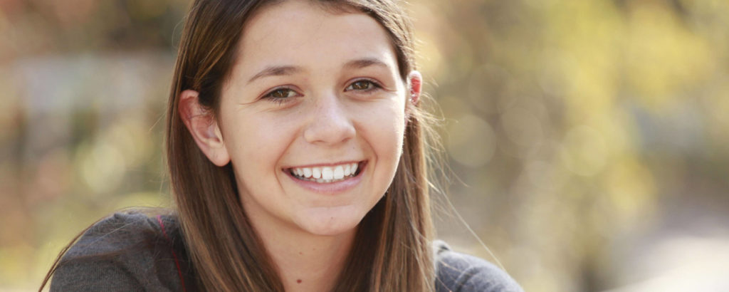 A teenage girl smiling  with healthy teeth, representing the benefits of pit and fissure sealants for cavity prevention