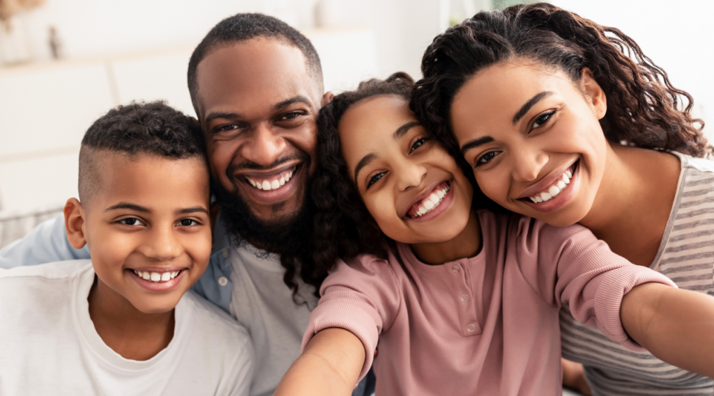 Smiling family of four taking a close-up selfie together at dental clinic